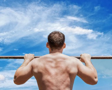 Güçlü atlet Pull-up yatay çubuğu'nda yapıyor. Closeup görünümü. Fitness, mavi gökyüzü arka plan mans.