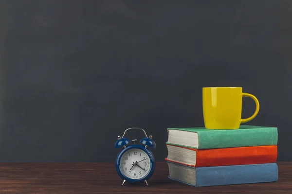 Stack of colorful textbooks on a wooden table, cup of coffee and alarm clock. Back to school.