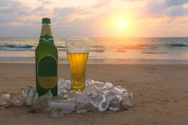 Bouteille brouillée et verre de bière Chang froide sur le sable à l'arrière-plan du paysage marin, du ciel couchant et des vagues de la mer . — Photo