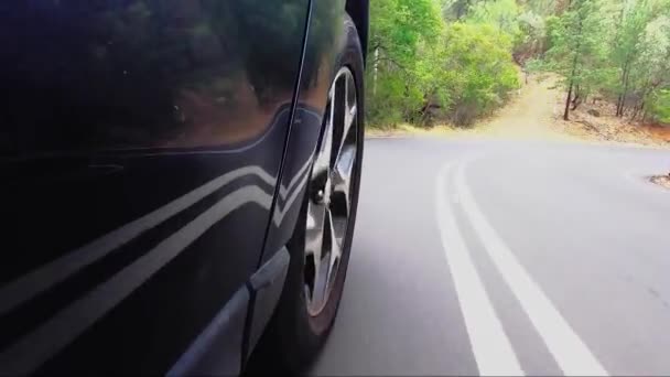 Car POV from road facing front right wheel driving down bitumen road down a hill into town