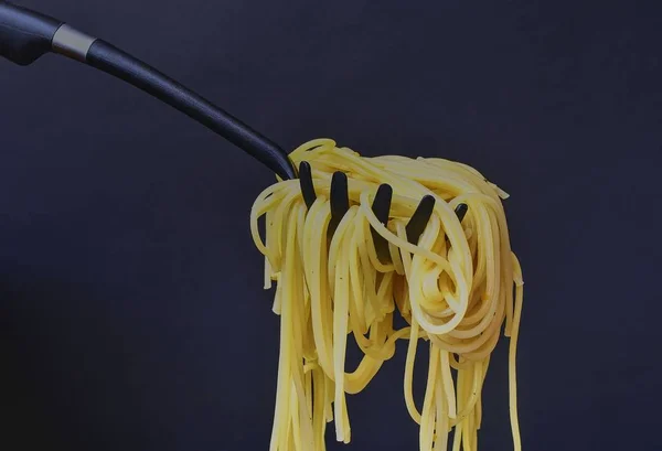 在意大利面条勺上煮的意大利面条。黑色背景的意大利面。特写。深色食品照片。复制空间 — 图库照片