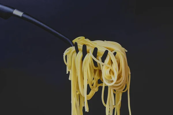 Spaghettis cuits sur une cuillère à spaghettis. Spaghetti sur fond noir. Photo de nourriture sombre. Espace de copie — Photo