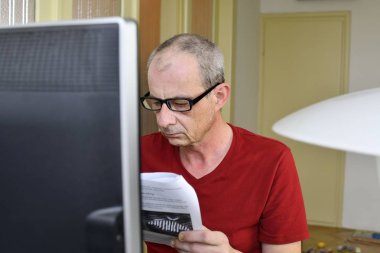 Orta masa başında oturan gözlüklü adam yaşlı. Kişisel bilgisayar kullanan olgun adam. Üst düzey kavramı. İnsan ve kırtasiyecilik. Dalgın adam evde çalışma office