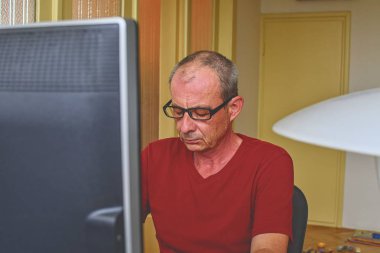 Orta masa başında oturan gözlüklü adam yaşlı. Kişisel bilgisayar kullanan olgun adam. Üst düzey kavramı. Evde office çalışan adam