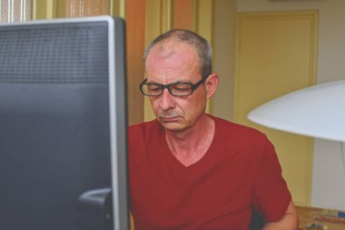 Orta masa başında oturan gözlüklü adam yaşlı. Kişisel bilgisayar kullanan olgun adam. Üst düzey kavramı. Evde office çalışan adam. 
