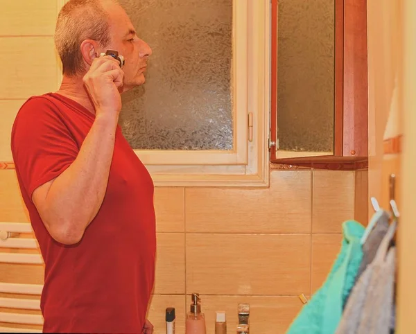 Orta bir banyoda tıraş, tıraş kullanarak adam yaşlı. Olgun adam evde. Üst düzey kavramı. 