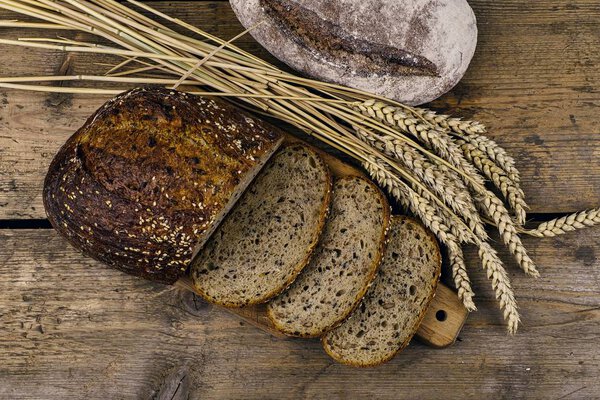 Булки хлеба, ломтики хлеба и колосья зерна на деревянном фоне. Сельская и сельская концепция. Закрыть
.  