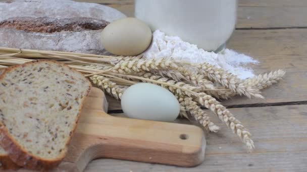 Mocos de pan, rebanadas de pan, harina de trigo, huevos y espigas de grano sobre fondo de madera. Concepto rústico y rural. De cerca. Puesta plana — Vídeo de stock