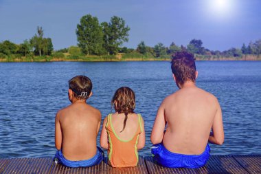 İskelede oturan çocuk. Yaz ve çocukluk kavramı. Çocuklar göle