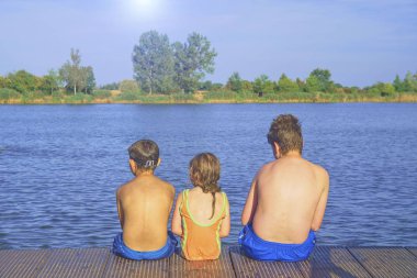 İskelede oturan çocuk. Üç farklı yaş çocuklar - genç çocuk, İlköğretim yaş çocuk ve ahşap bir iskele üzerinde oturan okul öncesi kız. Yaz ve çocukluk kavramı. Çocuk bankta göle