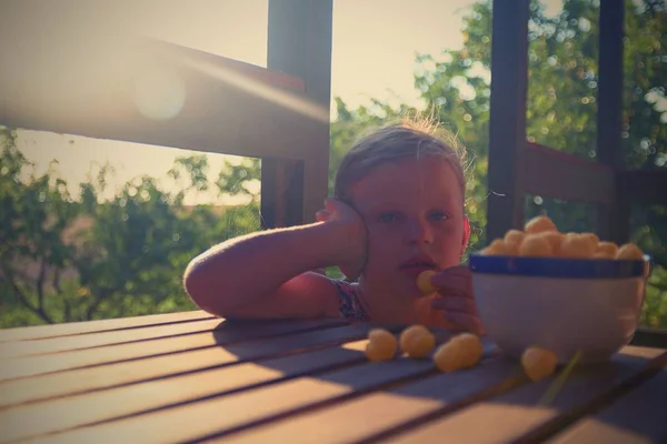 Malá dívka sedí na verandě v létě. Sýrové koule v misce. Sýr s příchutí občerstvení na stole. Snový a romantický obraz. Léto a šťastné dětství koncepce — Stock fotografie