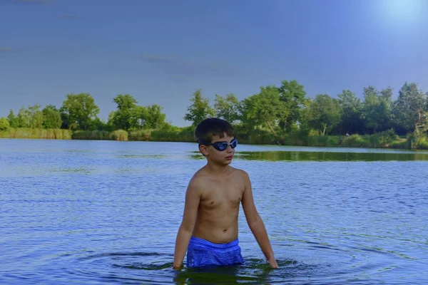 Söt liten pojke med SIM glasögon står i sjön på sommar dagen. Sommar och lycklig barn dom koncept. Kopiera utrymme i klarblå himmel — Stockfoto