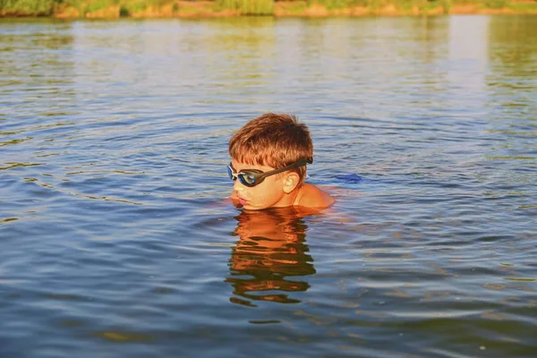 Lindo niño con gafas de natación nadando en el lago en el día de verano. Verano y concepto de infancia feliz. Copiar el espacio en agua azul brillante —  Fotos de Stock