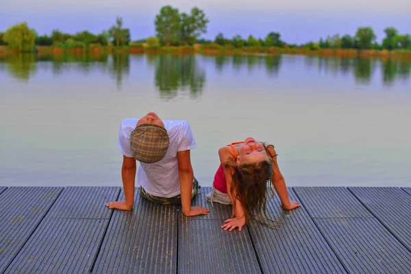 Küçük kız ve erkek düz kapak ile iskelede oturuyor. Erkek ve kız yukarı doğru gökyüzü üzerinde arıyoruz. Sevgi, dostluk ve çocukluk kavramı. Güzel romantik günbatımı resim
