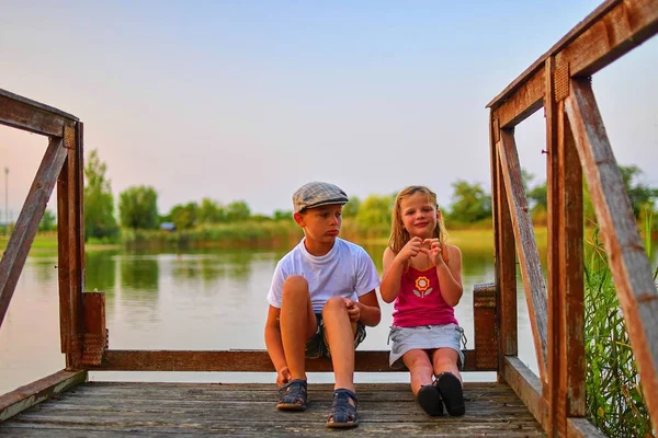 İskelede oturan çocuk. İki farklı yaş - İlköğretim çocuklarının ahşap bir iskele üzerinde oturan kız çocuk ve okul öncesi yaş. Kız kalp şekil verme. Yaz ve çocukluk kavramı. Çocuklar göle bankta. Retro filtre eklendi. 