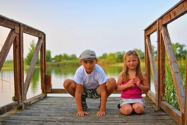 İskelede oturan çocuk. İki farklı yaş - İlköğretim çocuklarının ahşap bir iskele üzerinde oturan kız çocuk ve okul öncesi yaş. Yaz ve çocukluk kavramı. 