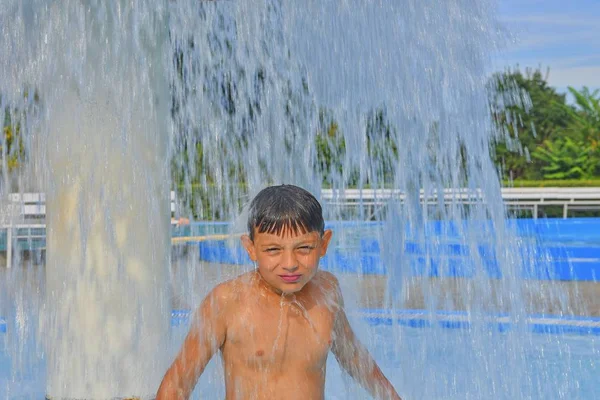 Little boy in the small swimming pool. Boy taking shower in water park. Boy standing under sprinkler in  spray pool. Summer and happy chilhood concept.