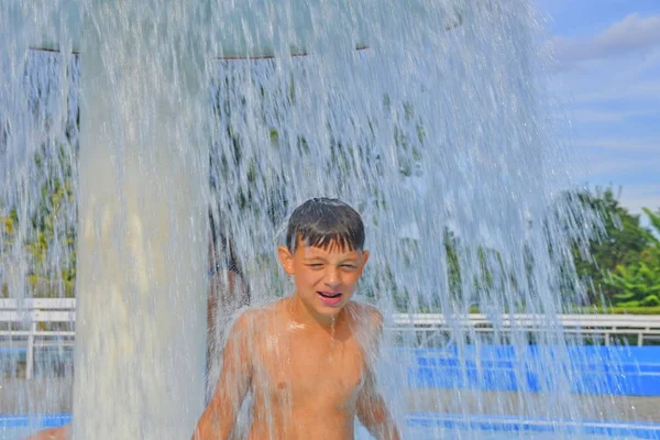 スイミング プールで夏の日を楽しんで幸せな少年 スプレー プールでスプリンクラーの下で立っている少年 夏と幸せ Chilhood コンセプト — ストック写真