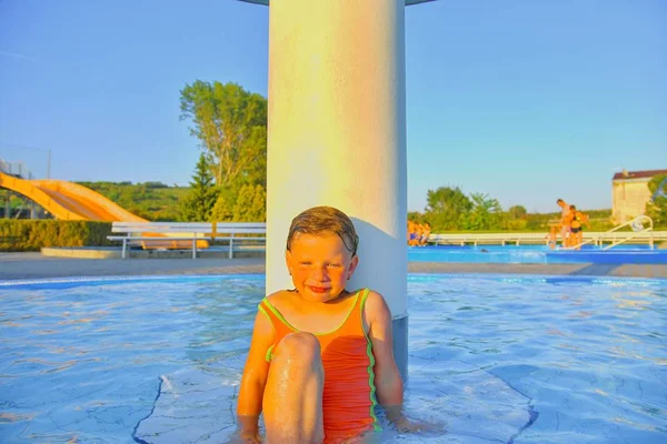 スプリンクラー スイミング プールでのシャワーの下で座っている女の子 スイミング プールでかわいい女の子の肖像画 晴れた夏の日 夏と幸せ Chilhood コンセプト — ストック写真