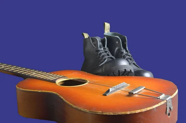 Rock and roll concept. Black boots and acoustic guitar. Rock and roll boots on navy blue background — Stock Photo, Image