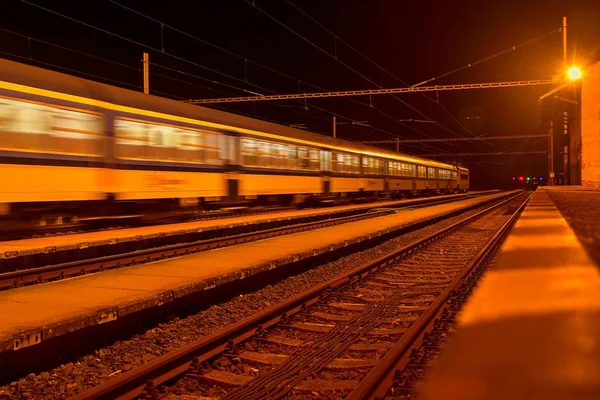 Bílá a modrá vlak projíždějící bez střechy malé nádraží v noci v České republice. Rozmazaného pohybu vlaku — Stock fotografie
