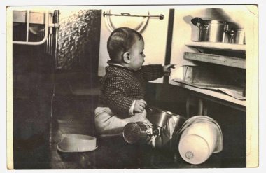 Vintage Fotoğraf tencere ile oynarken küçük yürümeye başlayan çocuk gösterir. Eşya dolabı üzerinden pişirme dışarı çekerek yürümeye başlayan çocuk. 
