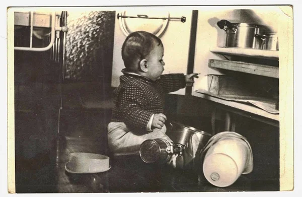 Foto vintage mostra pequena criança brincando com utensílios de cozinha. Criança retirando utensílios de cozinha do armário . — Fotografia de Stock