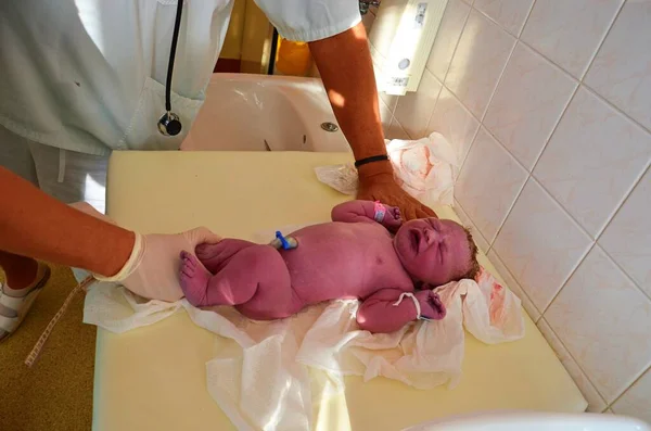 New born baby - girl with remainder of umbilical cord after successful childbirth. Real birthing and new born baby in a hospital. A healthy female newborn baby girl has been examined and takeing the