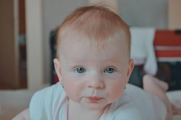 Petite fille mignonne s'allonge sur le lit en souriant. Petite fille de 6 mois. Portrait d'une petite fille sur le lit dans la chambre. Chambre domestique — Photo