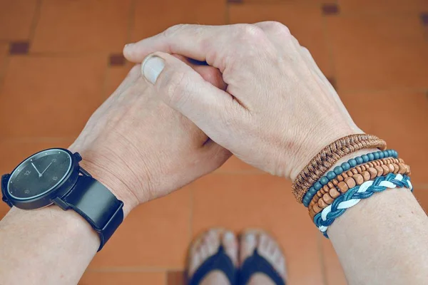 Man wearing a bracelet made of rope, wood, leather, beads and colored rope sack. Black watch on man hand. Hipster fashion on tiled flooring background