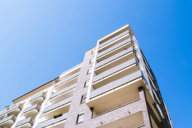 Üst üste yığılmış balkonları ve temiz geometrik tasarımı olan modern yerleşim yerleri açık mavi gökyüzüne karşı yükseliyor..