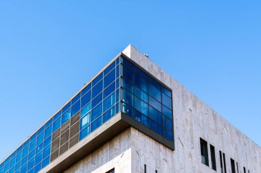 Çağdaş ofis binası. Yansıtıcı mavi pencereleri, beyaz perisi ve parlak gökyüzü altında minimum sarı aksanları var..