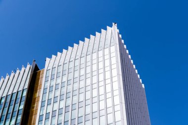 Pürüzsüz dikey çizgileri ve açık mavi gökyüzüne karşı yükselen cam perili modern yüksek katlı ofis kulesi..