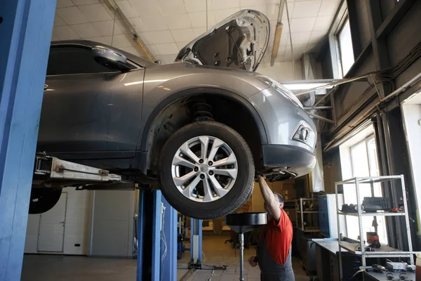 Car Mechanic Fixing Tie Rod and Steering System While Being Under the Vehicle. Car Maintenance in the Professional Service.