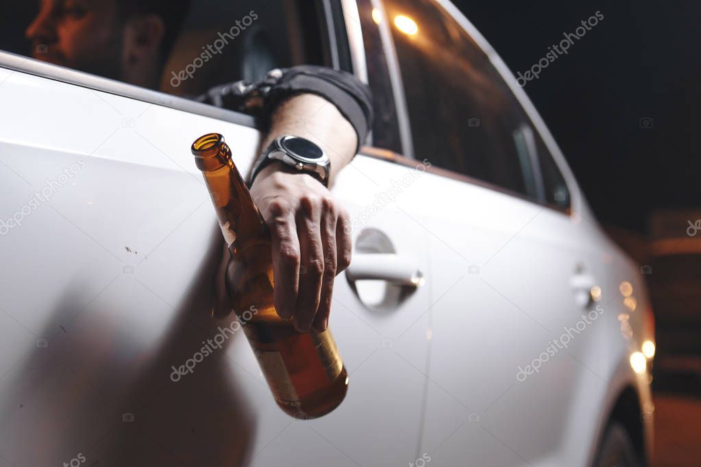 Drunk young man drives a car with a bottle of beer. This is a campaign picture of Dont Drink for Drive. 