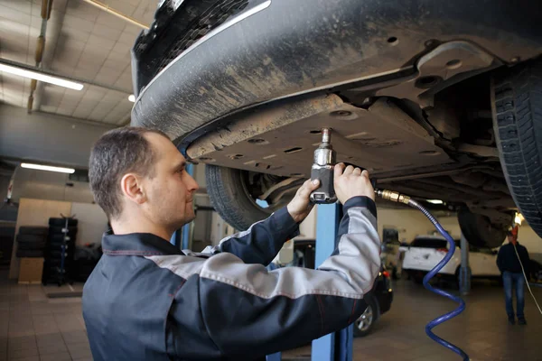 Porträtt av en mekaniker som reparerar en upplyft bil — Stockfoto