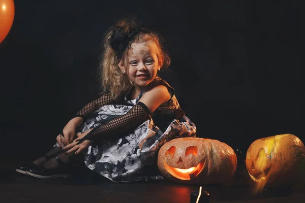Grappige kind meisje in heks kostuum voor Halloween met pompoen Jack en oranje ballon op een donkere houten achtergrond — Stockfoto