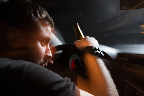 Мужчина пьяный водитель пьет пиво на фоне освещения полицейской машины. Вождение под воздействием алкоголя — стоковое фото