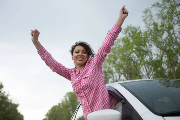 Симпатична смішна молода жінка вішає голову з машини через відкрите вікно насолоджуючись свободою вітру в її волоссі, коли вона рухається вздовж сільської місцевості — стокове фото