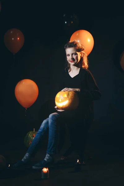 Halloween-Hexe mit geschnitztem Kürbis und magischen Lichtern in einem dunklen Wald. schöne junge überraschte Frau in Hexenhut und Kostüm mit Kürbis. Halloween-Party-Kunst — Stockfoto