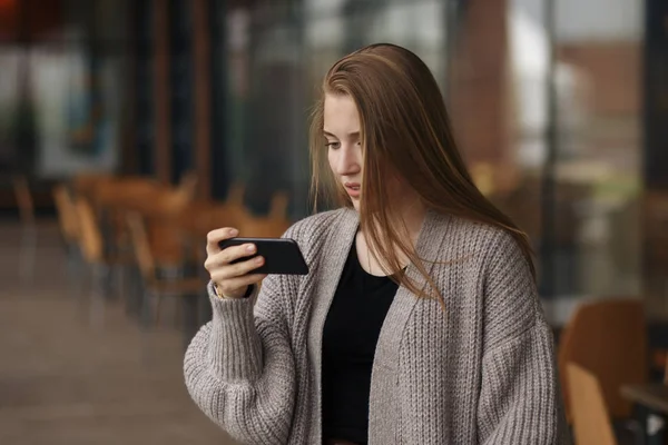 Donna felice utilizzando uno smartphone in strada con uno sfondo sfocato — Foto Stock