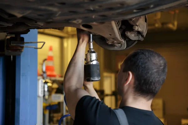 Car Mechanic Fixing Tie Rod and Steering System While Being Under the Vehicle. Car Maintenance in the Professional Service.