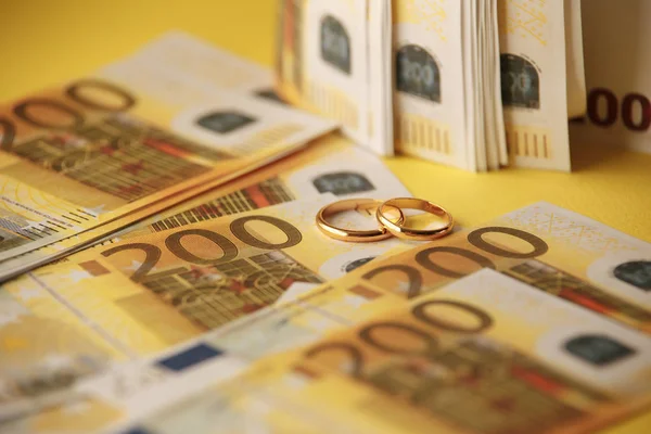 Two wedding rings and money as symbol for an expensive alliance — Stock Photo, Image