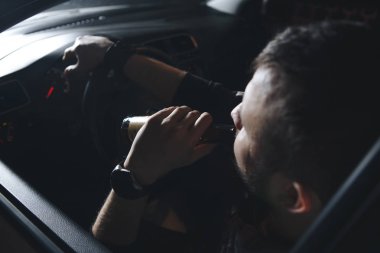 Yakışıklı genç bir adam ile bir şişe bira veya düşük alkol içki bir araba direksiyonda sakallı. Bağımlılık yapan maddeler bir durumda sürüş