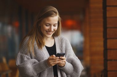 Alışveriş çantası seyir telefon güneşli sonbahar gününde olan kadın.