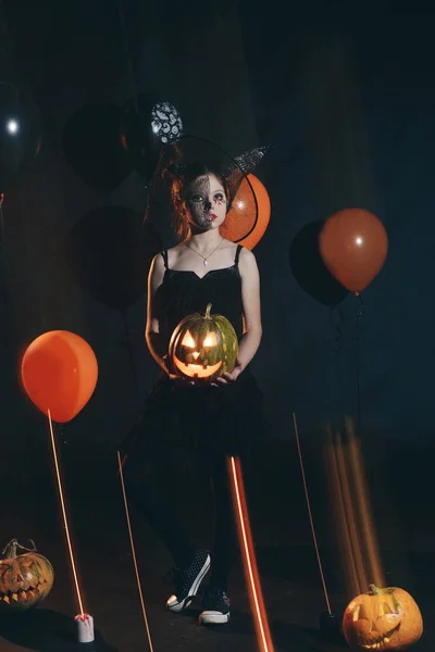 Süßes und hübsches Mädchen mit langen Locken, das für Halloween mit einem riesigen schwarz-orangen Hut posiert — Stockfoto