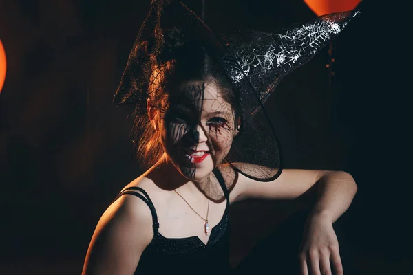 Bonito e bonito menina com longos cachos posando para halloween vestindo um enorme chapéu preto e laranja — Fotografia de Stock