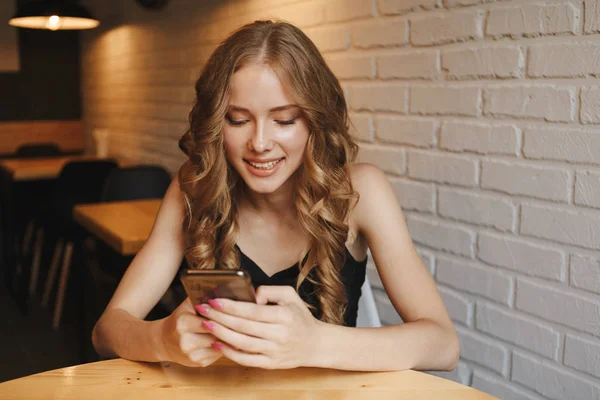Ritratto di una donna bionda carina leggere qualcosa sul suo smartphone mentre seduto nel caffè moderno — Foto Stock