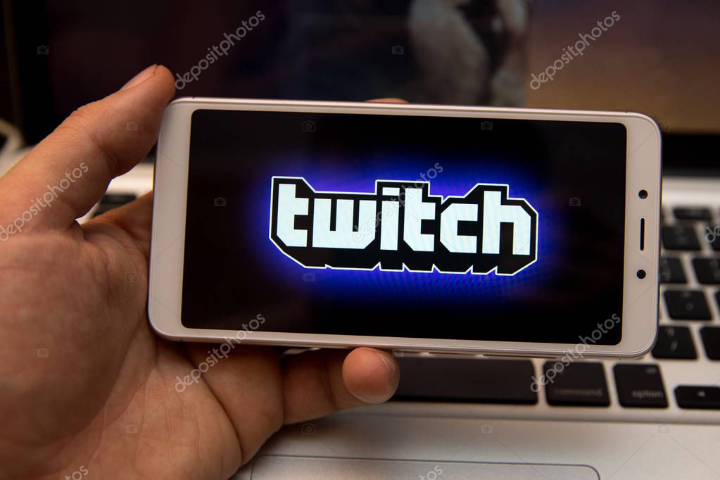 Tula, Russia - October 31, 2018:: A Man holds edge Mobile Phone with Twitch application on the screen in coffee shop. Twitch is a live streaming video service