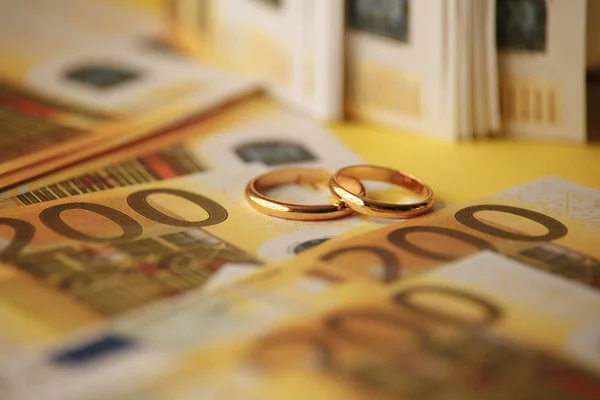Two wedding rings and money as symbol for an expensive alliance. Golden wedding rings on euro banknotes — Stock Photo, Image